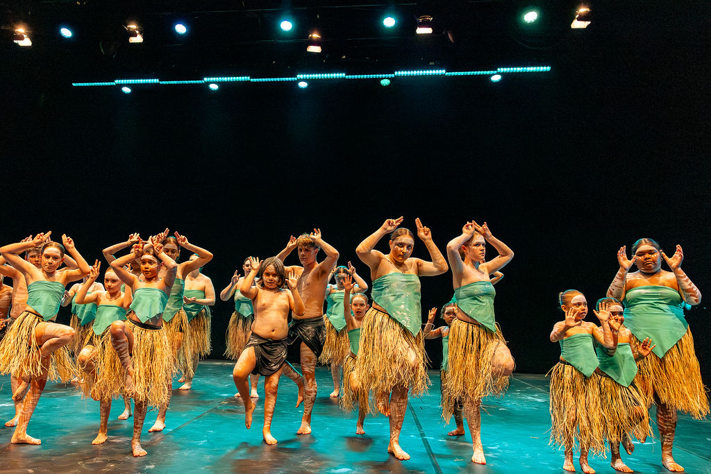 A group of indigenous dance performers on a darkened theatre stage