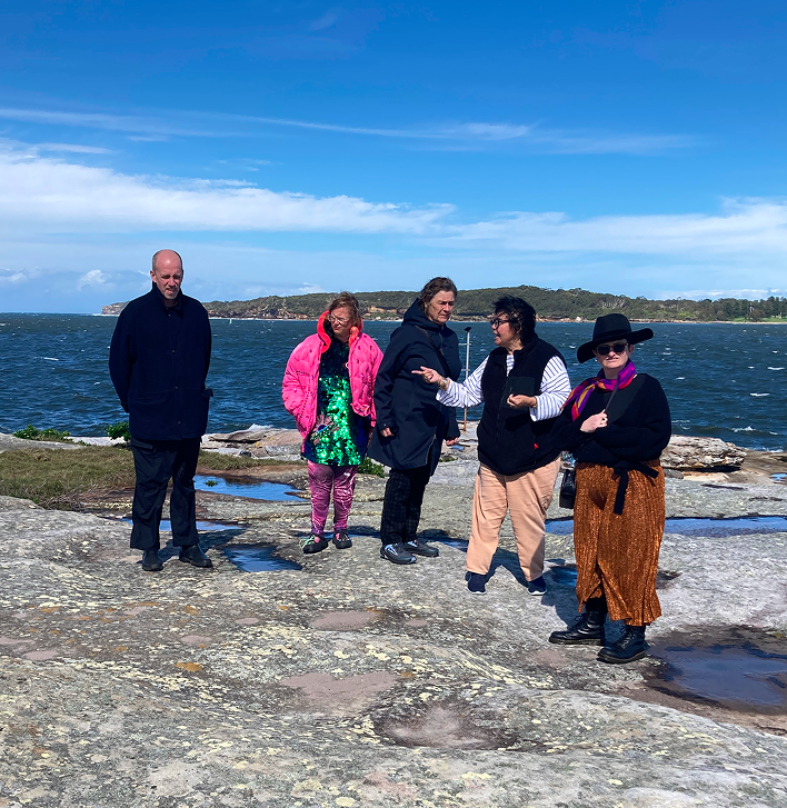 A group of artists gather near the ocean with an Indigenous Elder showing and sharing Country