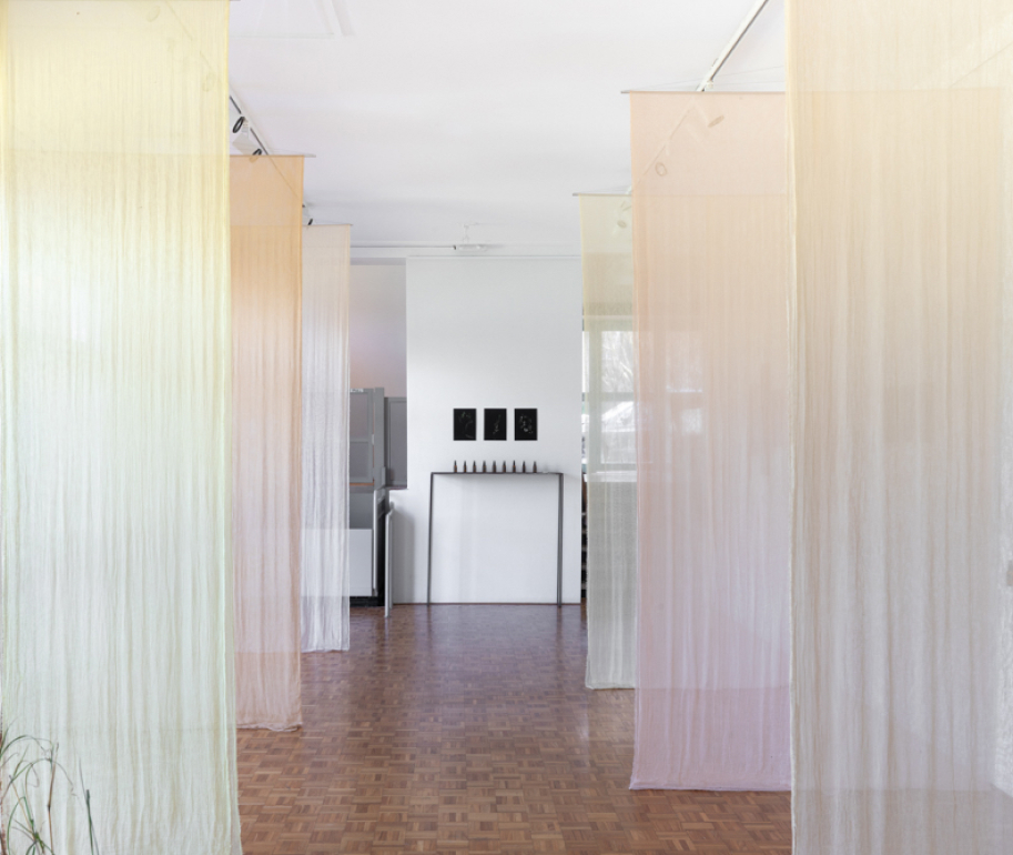 An installation of light cloth hanging from the ceiling that has been dyed with plant material 